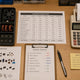 Top-down editorial photograph of a planning workspace with quarterly budget spreadsheet (Q1-Q4 columns visible), calculator with paper tape, printed parts catalogue.