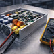 Antminer APW12 power supply unit opened on a workbench next to a digital multimeter, illustrating the PSU diagnosis procedure with DC output testing.